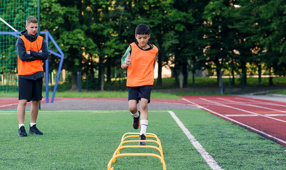 A student performing agility ladder drills with a sports coach on the training field at Chowgule International School, Goa.